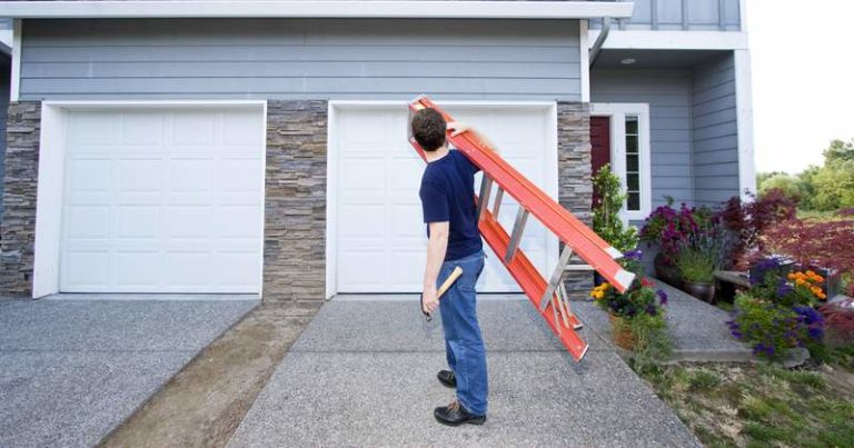 Man holding ladder and hammer in front of two car garage